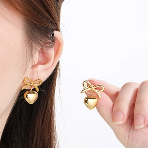 Detail of golden bow and heart drop earrings with polished finish and elegant design