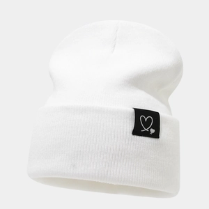 Gros plan du bonnet blanc en maille côtelée avec un écusson noir à broderie de cœur