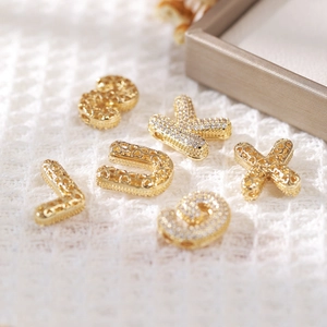 Gold plated puffy alphabet necklaces with zircon charms on a textured fabric background