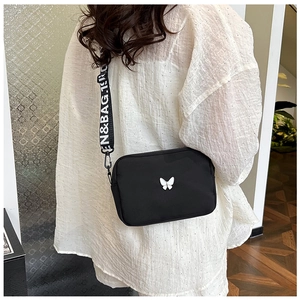 Detail view of black nylon crossbody bag with white bow accent and lettered wide strap