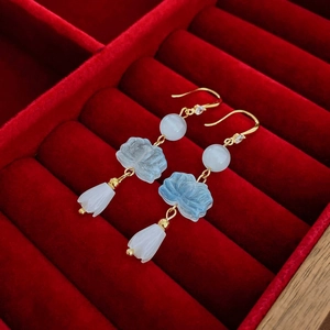 Detail of gold-plated lotus earrings with blue beads and white flower charms on red velvet