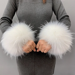 A pair of large white faux fur cuffs worn over a grey long sleeve dress on a grey backdrop