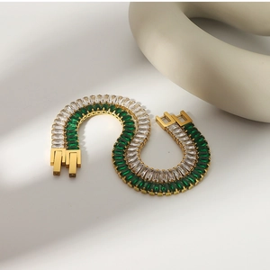Detail of emerald and white zircon gold bracelets arranged in an S-shape layout