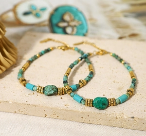Detail of bohemian turquoise and gold bead bracelet on a light beige stone background