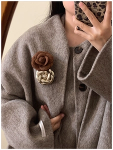 Detail of brown fabric flower and gold metal brooch on a grey wool coat lapel