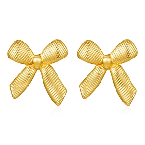 Detail of gold bow earrings featuring a textured striped surface and polished metallic finish