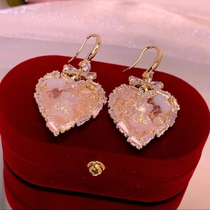 Macro detail of heart-shaped earrings with bear motif and crystals on red velvet box