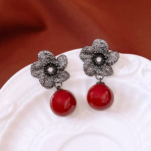 Close-up of vintage flower drop earrings with red beads on a white embossed porcelain plate