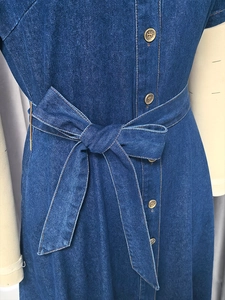 Dettaglio di un abito di jeans con fiocco in vita e bottoni metallici su un manichino