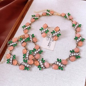 Detail of vintage jewelry set with pink stones and green leaf gems on gold metal base