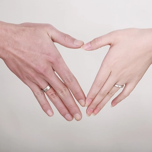 Close-up of couples hands forming a heart shape wearing silver stainless steel rings