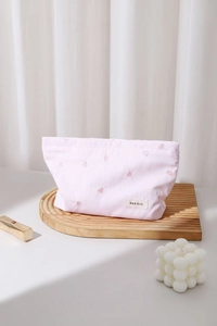 Detail of pink striped makeup bag with heart embroidery on a wooden tray with lipstick
