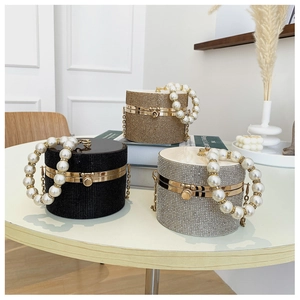 Chic cylindrical evening bags with rhinestones and pearl handles on a table