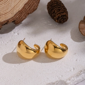 Polished gold teardrop stud earrings for women displayed on a natural textured stone base