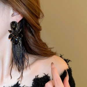Detail of long black feather earrings with crystals and tassels on a female model