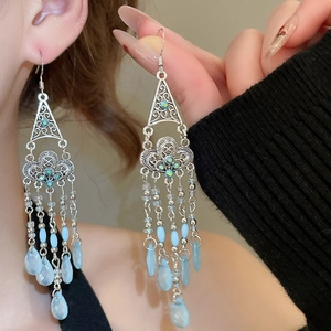 Detailed close-up of ethnic style silver tassel earrings with light blue beads on a model
