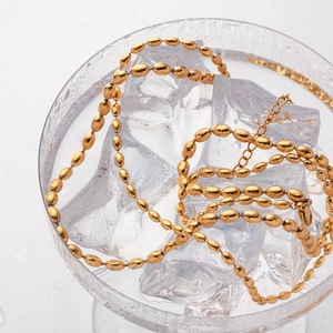 Close-up of golden stainless steel beaded chain necklace on ice cubes with white background