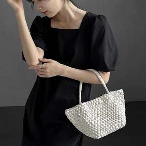 Detail of a white hand-woven dumpling bag carried by a model in a black dress