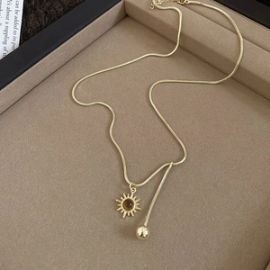 Detailed macro of golden sun pendant with brown bead on sleek snake chain jewelry