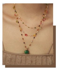 Détail d'un collier de perles doré multicouche avec un pendentif ovale en pierre verte