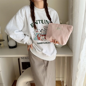 Close-up of a pink corduroy makeup bag held by a model in a cozy, bright room setting