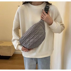 Close-up of gray quilted crossbody bag with adjustable black buckle strap on model