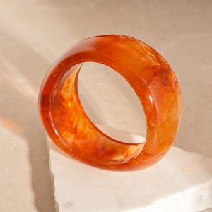 Detail of translucent orange resin bangle with a marble texture on white stone