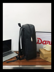 Side view of black leather texture backpack on a bench with laptop and zipper details