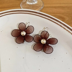 Detail of dark brown mesh flower earrings with rhinestones on a white ceramic plate