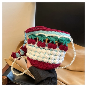 Close-up of handmade crochet bucket bag with red cherry accents and pearl shoulder strap