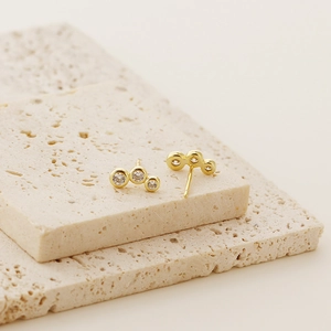Detail of gold geometric stud earrings with clear zircon stones on a beige stone plate