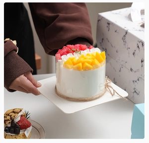 Close-up of white mousse cake with fruit toppings held by hands in front of a white box