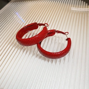 Detailed view of red textured hoop earrings with snake skin pattern on a white surface