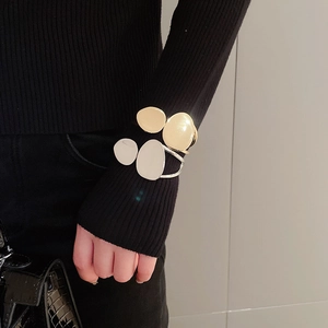 Detail of gold and silver irregular oval bangles worn over a black knitted sleeve