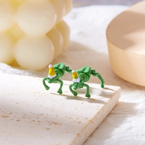 Creative green frog earrings with yellow Christmas hats on a decorative stone base