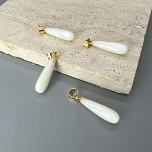 Colgantes de nácar blanco en forma de gota con cierres dorados sobre piedra texturizada