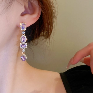 Detail view of long geometric earrings with purple stones and crystals on a model