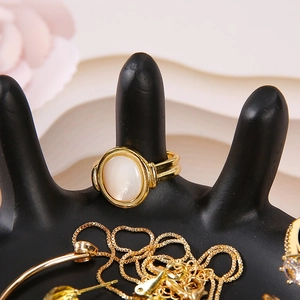 Detail of a gold ring with oval white shell gemstone on a black palm jewelry display stand