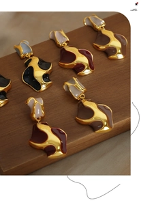 Detailed view of colorful enamel inlay on wavy geometric gold earrings set on wood