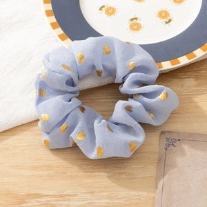 Detailed view of a blue fabric hair scrunchie featuring gold heart foil patterns