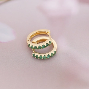 Elegant 18K gold-plated hoop earrings with vibrant green zircon stones on pink silk