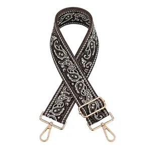 Adjustable brown paisley jacquard bag strap with gold metal buckles on white background