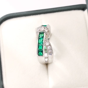 Detailed close-up of criss-cross silver ring featuring four emerald-green square gemstones