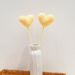Detail of yellow handmade crochet heart decorations in a white vase and woven basket