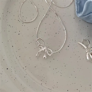 Detail of silver bow pendant on a fine snake chain necklace with small bead accents