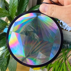 Close-up of circular rainbow suncatcher prism held against a natural green leaf background