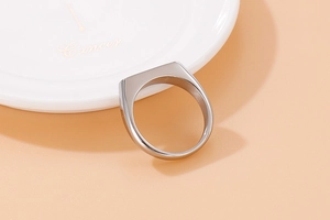 Polished silver stainless steel signet ring on white ceramic with orange background