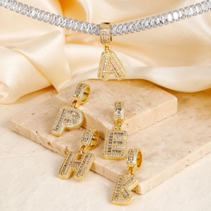 Close-up of golden letter pendants with sparkling zircon on soft beige silk background