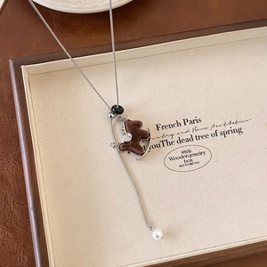 Close-up of a brown flocked bear pendant with silver crescent and pearl on a long chain