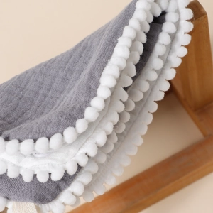 Close-up of grey cotton muslin baby bib with decorative white pom-pom trim detail